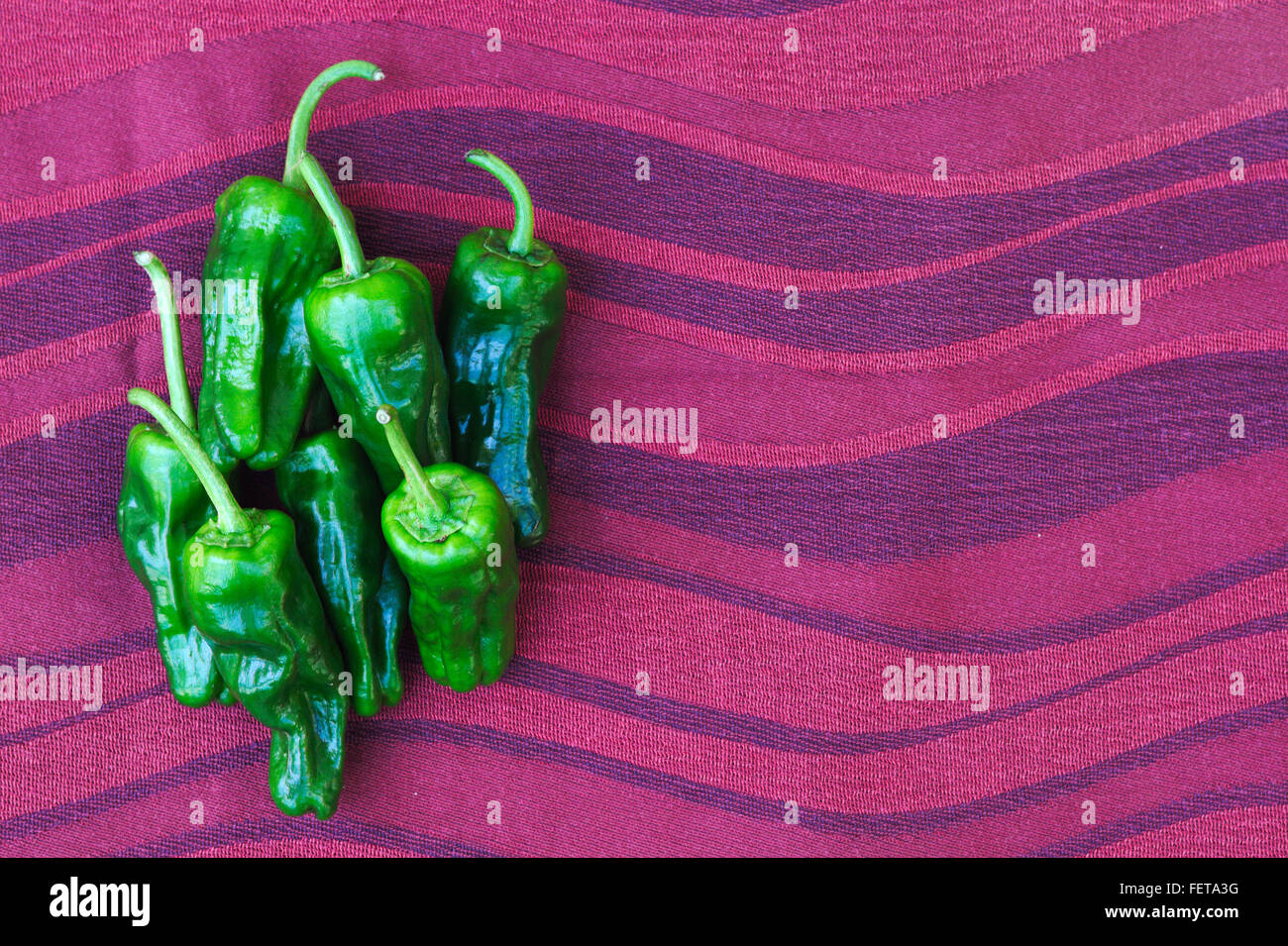Einen kleinen Stapel von sieben Mini-süße grüne Chilischoten auf rotem Stoff wellig Hintergrund. Stockfoto