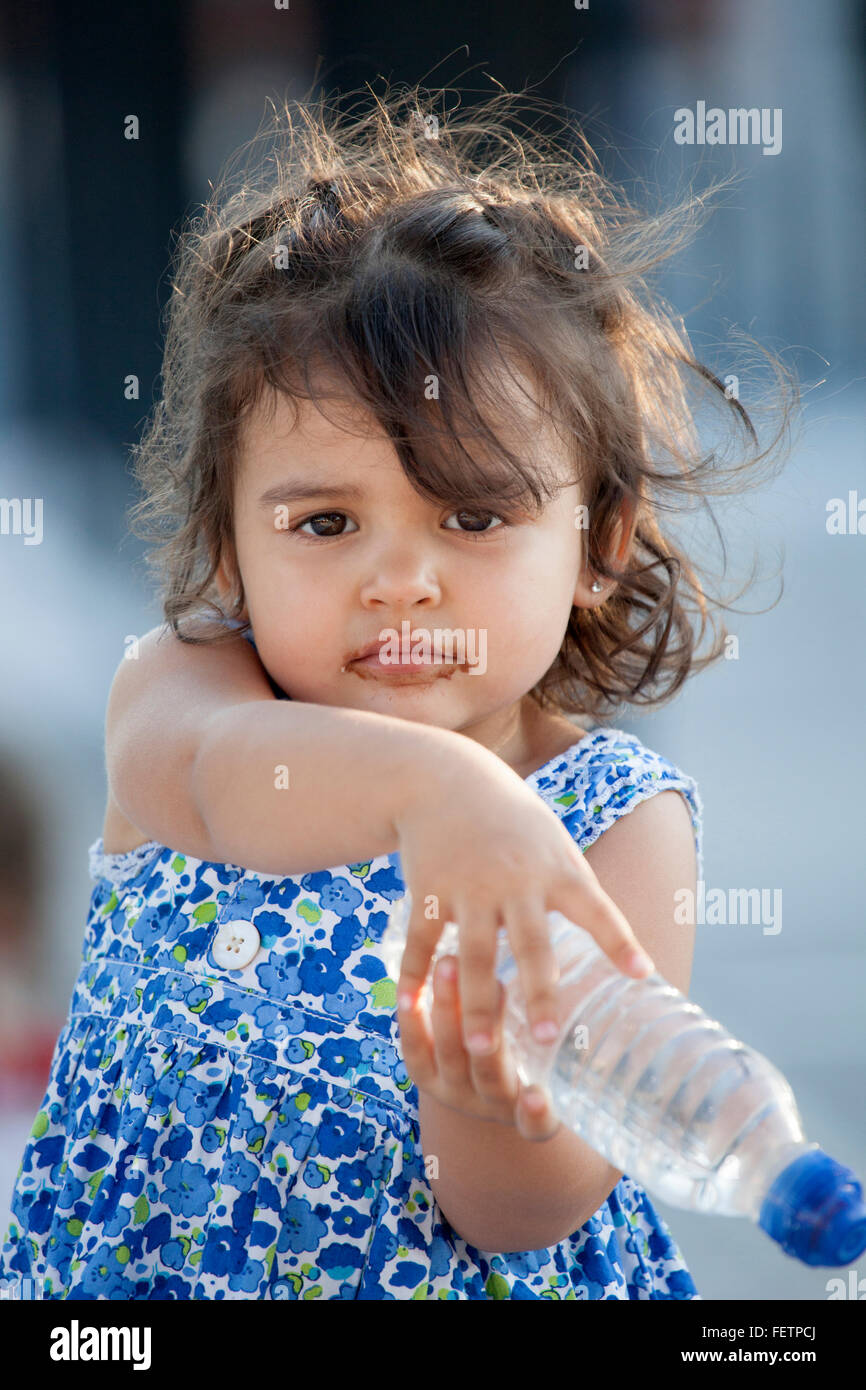 Hübsches kleines Mädchen mit Mund bedeckt mit Schokolade Blick in die Kamera halten Sie Flasche Wasser. Windigem Wetter Stockfoto