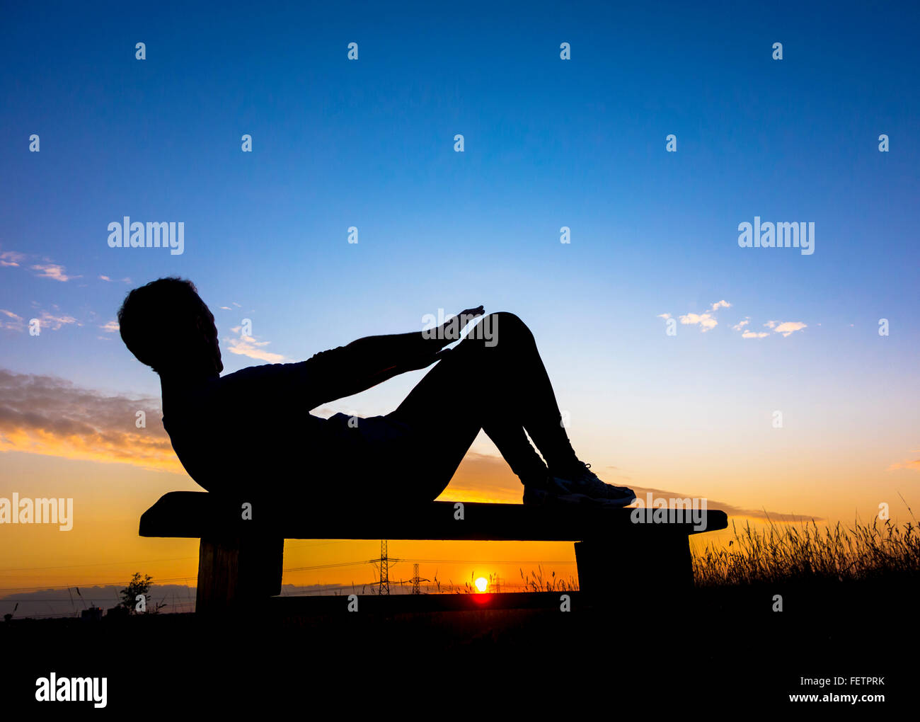 Jogger Erwärmung tun Sit Ups bei Sonnenuntergang in Woodland Park. Großbritannien Stockfoto