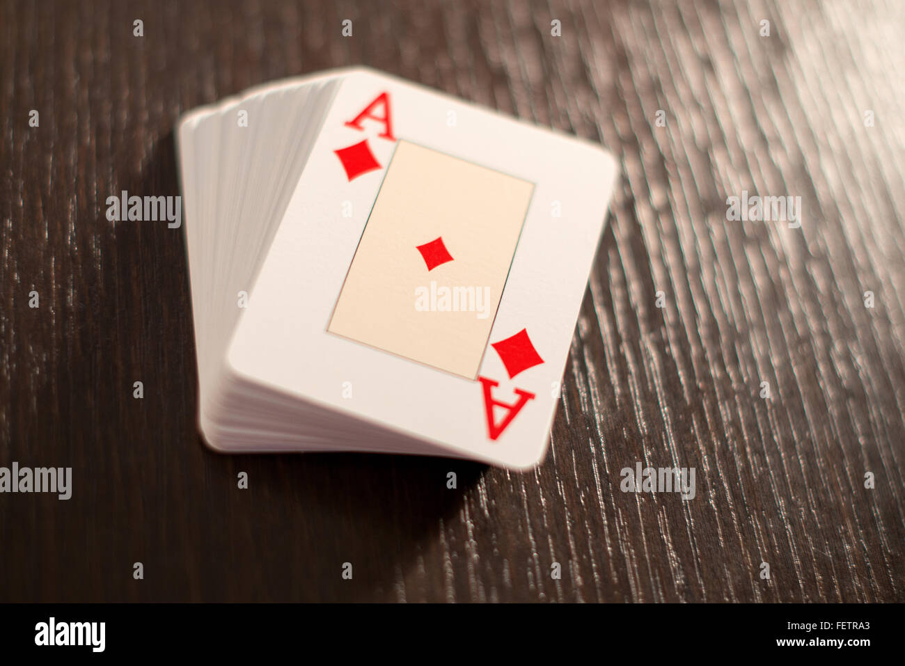 Gestapelte Kartenspiel zeigt das Karo-Ass auf der Oberseite eine strukturierte Holztisch mit Gegenlicht und Textfreiraum Stockfoto