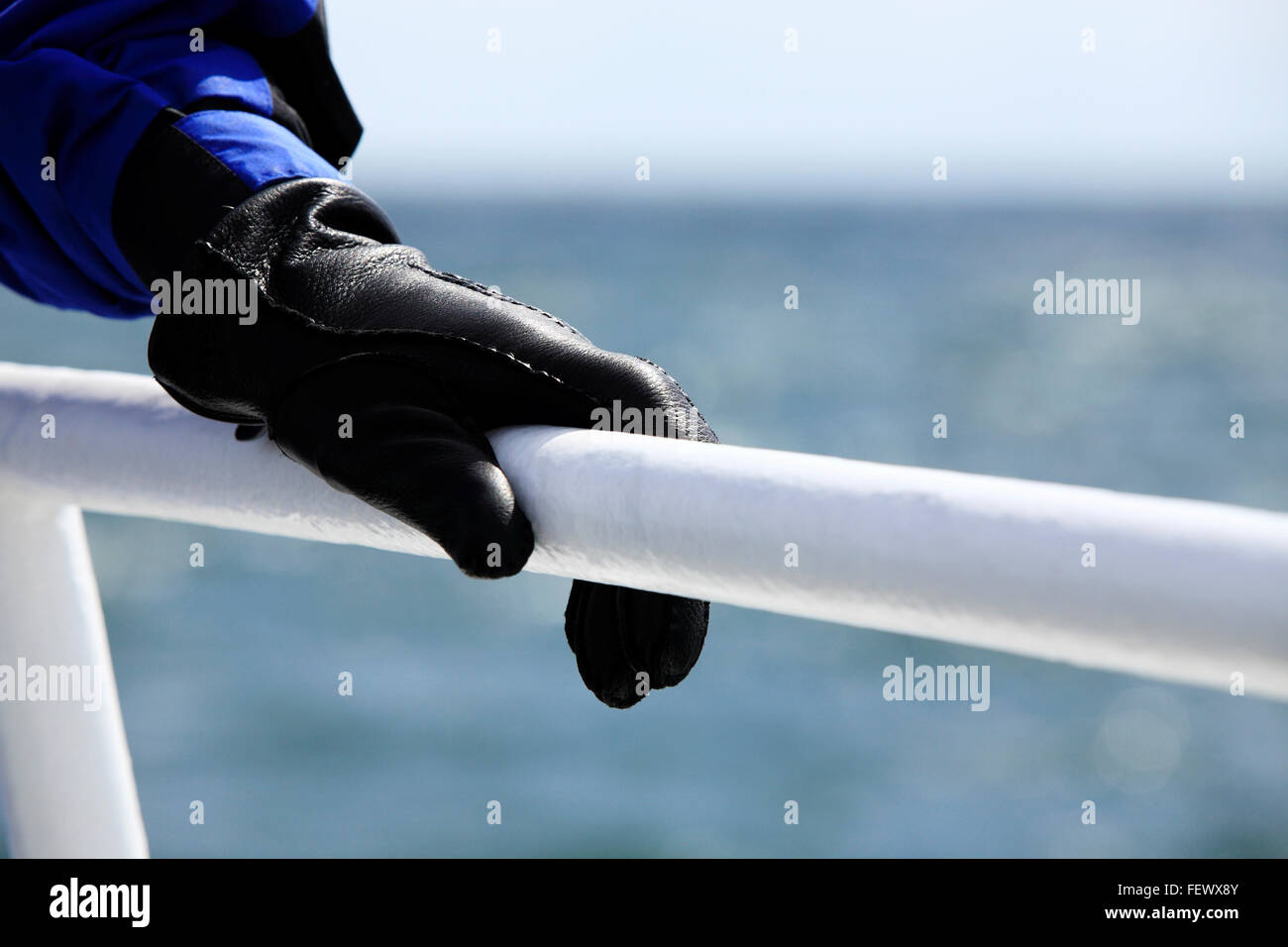 Hand, trägt einen schwarzes Leder-Handschuh festhalten an einem weißen Handlauf auf einem Boot Stockfoto