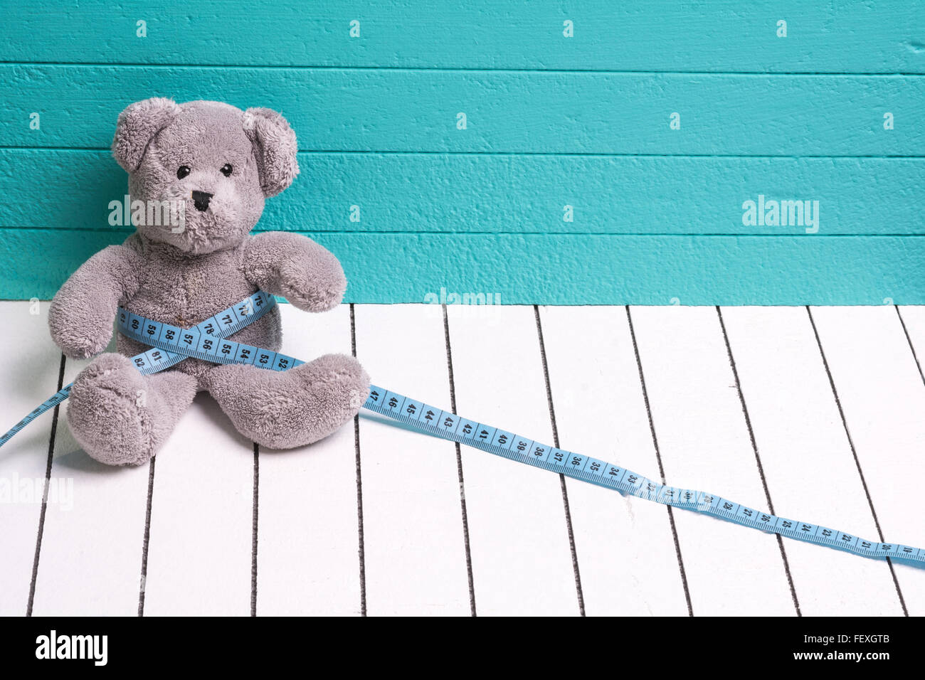Teddy-Bär auf einem weißen Holzboden blau-grünen Hintergrund mit Zentimeter. Ernährung und Gewicht Verlust bei Kindern Stockfoto