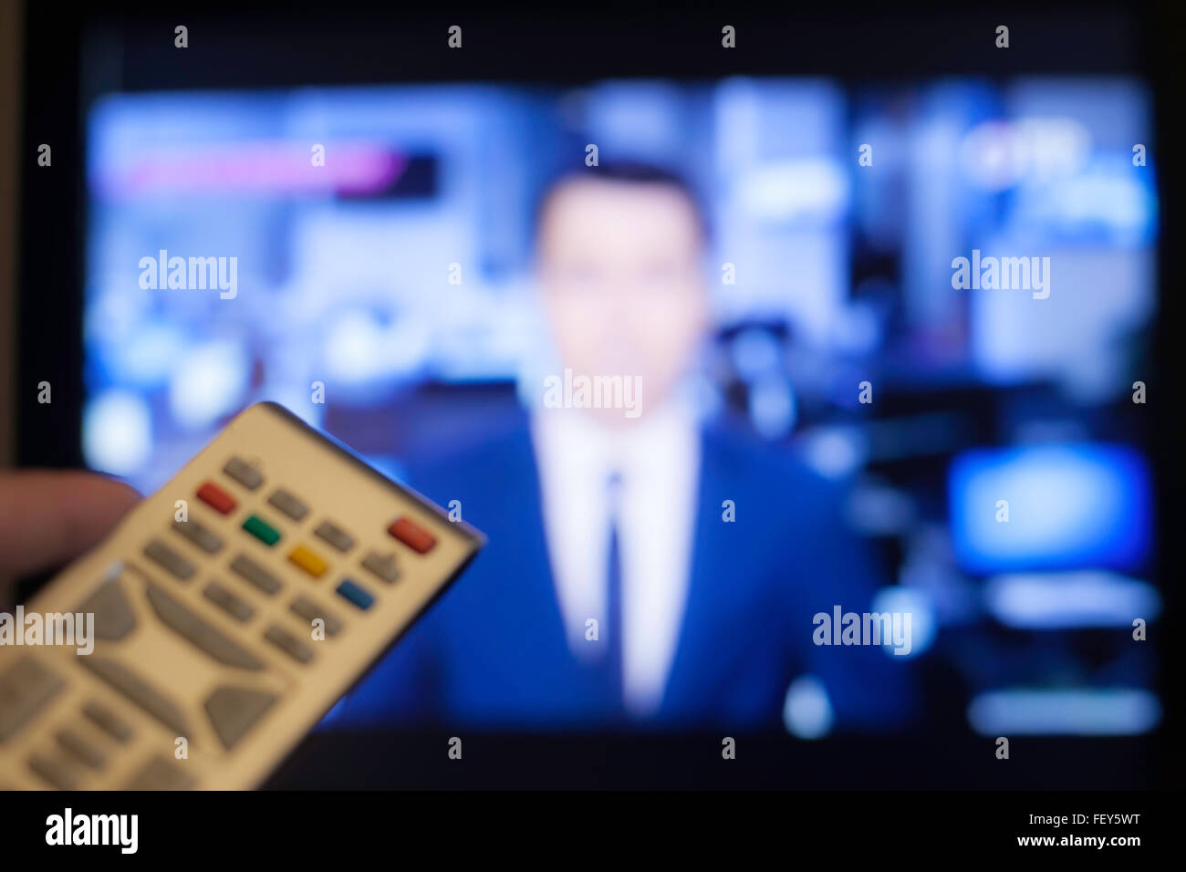Hand mit TV remote mit einem Fernseher im Hintergrund Stockfoto