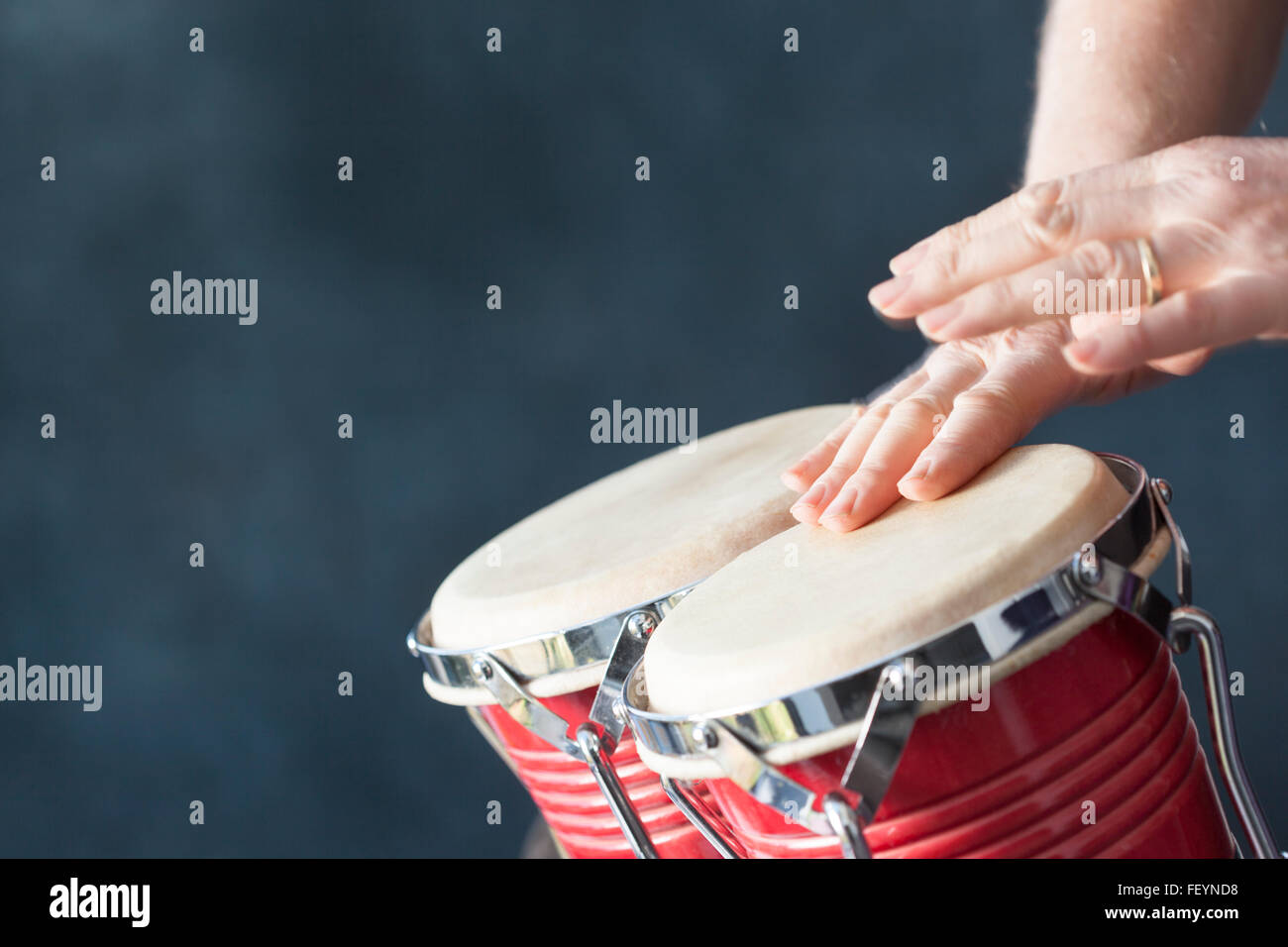 Hände spielen rote Bongo-Trommeln mit grauem Hintergrund Stockfoto