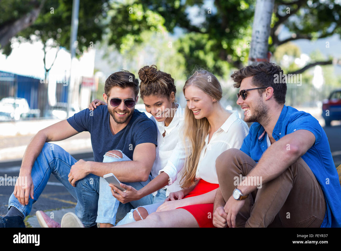 Hip Freunde Blick auf Smartphone und sitzen auf Bürgersteig Stockfoto