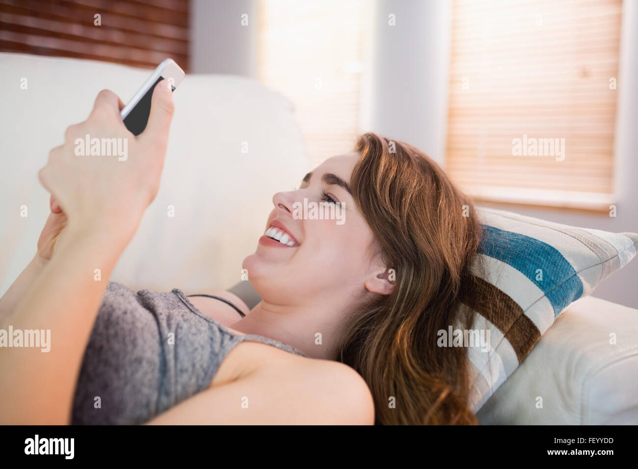 Hübsche Frau liegend auf der Couch mit Telefon Stockfoto