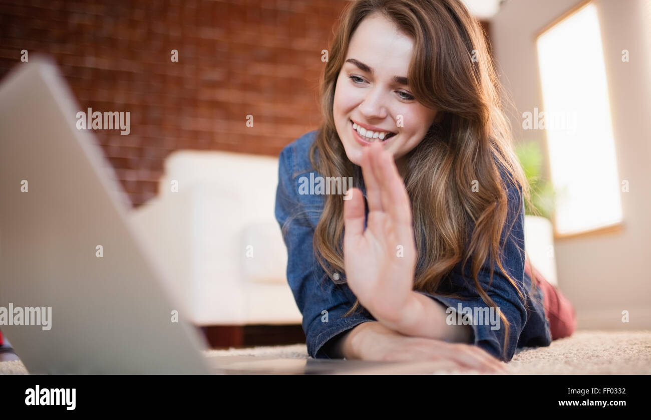 Ziemlich lächelnde Frau, die auf dem Boden winken am laptop Stockfoto