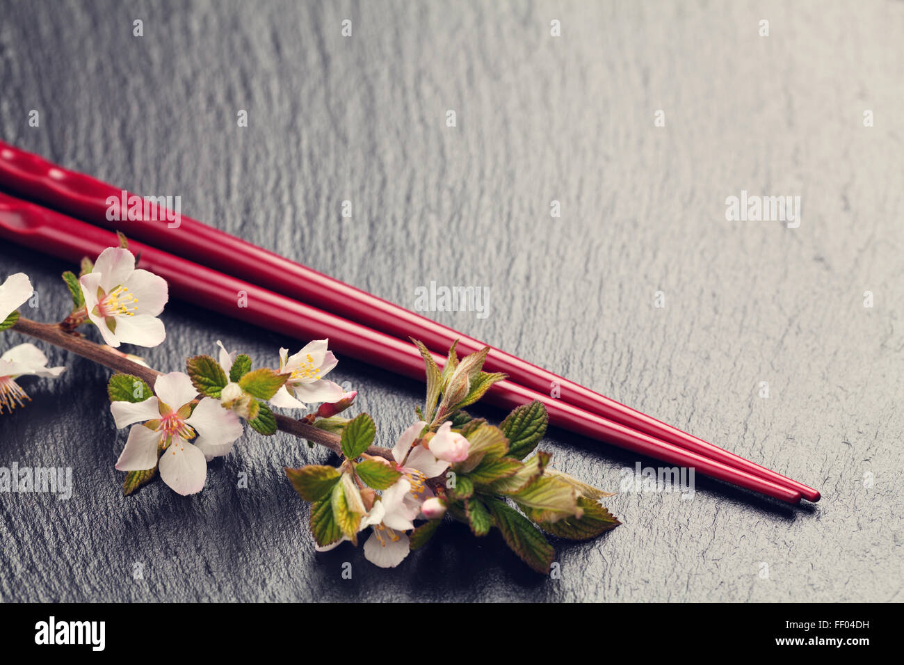 Japanische Sushi-Stäbchen und Sakura Blüte auf schwarzem Stein. Draufsicht mit Textfreiraum. Getönten Stockfoto