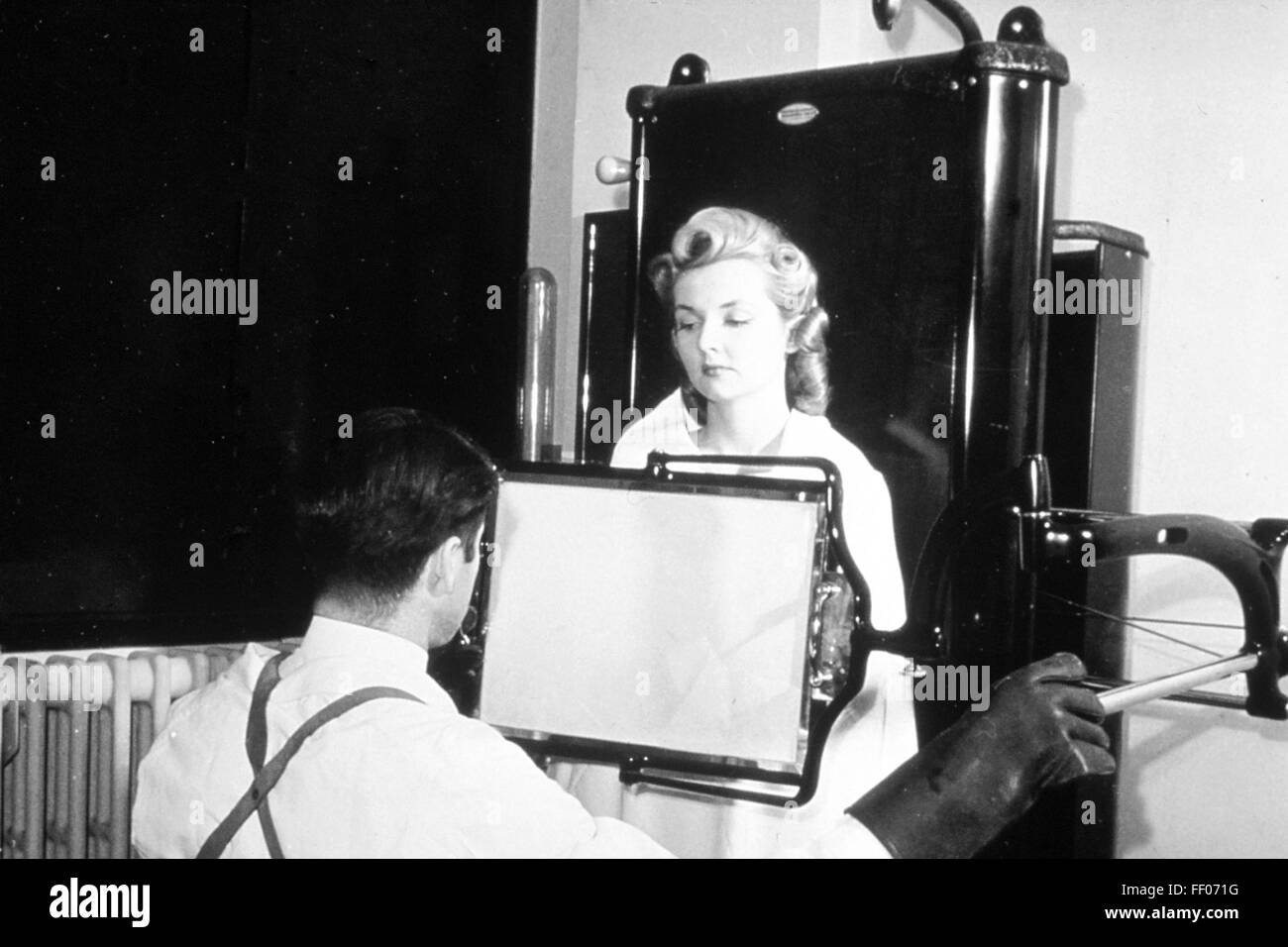 Röntgen-Techniker unter einer Röntgen-Fluroscope im Jahre 1940. Die Röntgenröhre ist hinter dem Patienten. Der Betreiber Glasscheibe hat eine fluoreszierende Beschichtung zeigt das Bild. Diese Technik bietet eine viel höhere Dosis der Strahlung als Filmbilder. Das Foto wurde verwendet, um die Idee entgegen zu wirken, dass diese Strahlung gefährlich war. Foto: National Cancer Institute of America Stockfoto