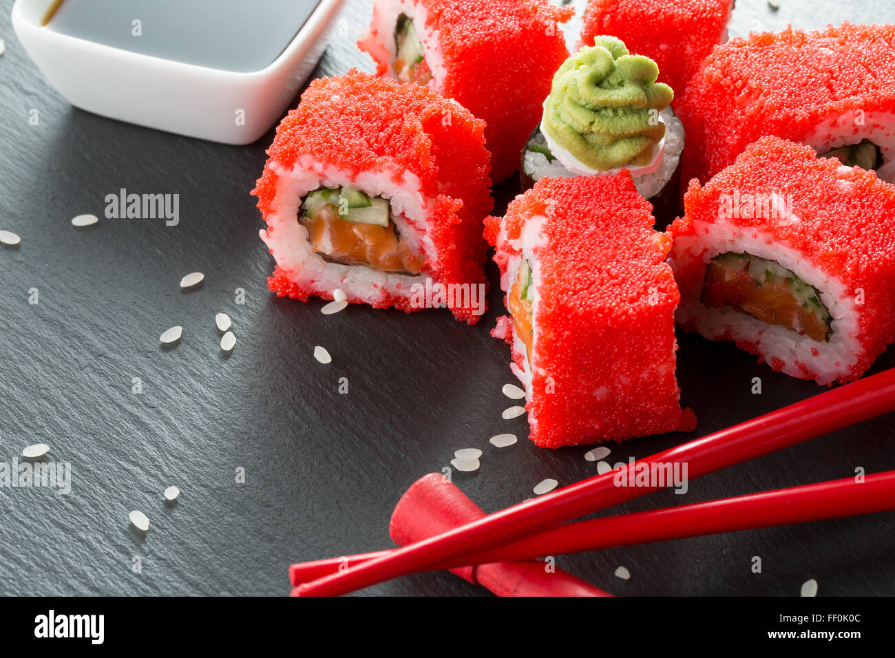 Sushi-Rollen mit roten Stäbchen und Sauce auf einem Schiefer Tisch. Stockfoto