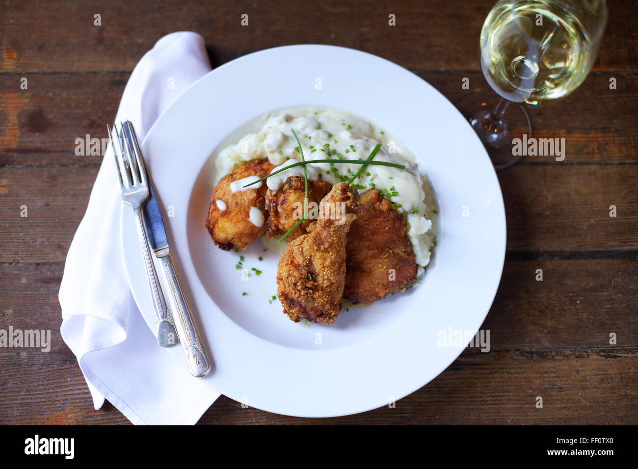 Ein Teller mit gebratenem Huhn und einer Seitenlänge von Kartoffelpüree mit einem Glas Weißwein von oben geschossen. Stockfoto