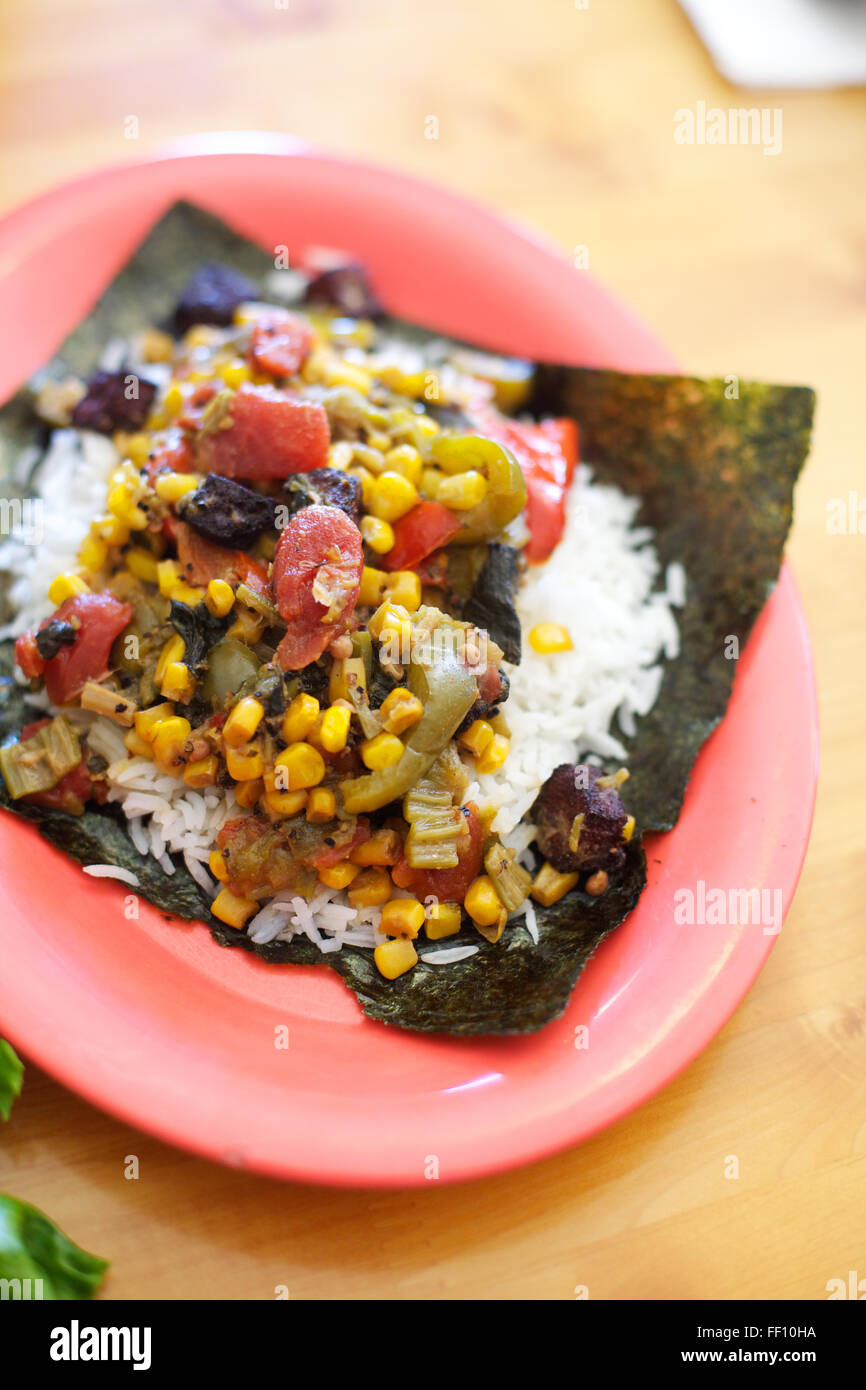 Eine gesunde Mahlzeit aus Reis mit Gemüse, serviert auf einem Blatt Nori Algen und auf einem hellen Lachs rosa Teller garniert. Stockfoto