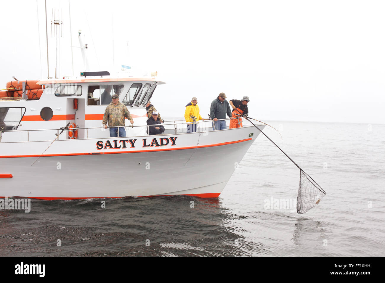 Eine Gruppe von Fischern Lachs Angeln auf einem gecharterten Boot auf ruhigem Wasser an einem grauen, nebligen Nachmittag. Stockfoto