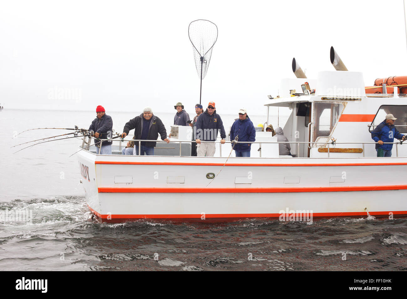 Eine Gruppe von Fischern Lachs Angeln auf einem gecharterten Boot auf ruhigem Wasser an einem grauen, nebligen Nachmittag. Stockfoto