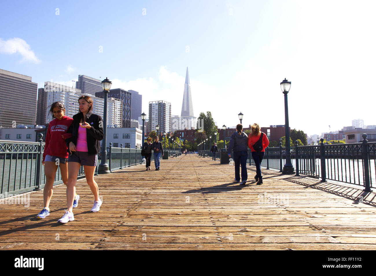 Menschen zu Fuß entlang der Pier 7 an einem sonnigen Tag auf San Franciscos Embarcadero mit der Transamerica Pyramide im Hintergrund. Stockfoto