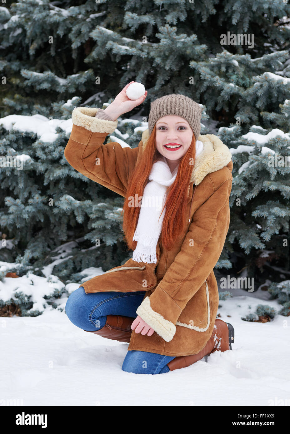 Mädchen spielen Schneebälle in Winter Park am Tag. Verschneite Tannen. Rothaarige Frau voller Länge. Stockfoto