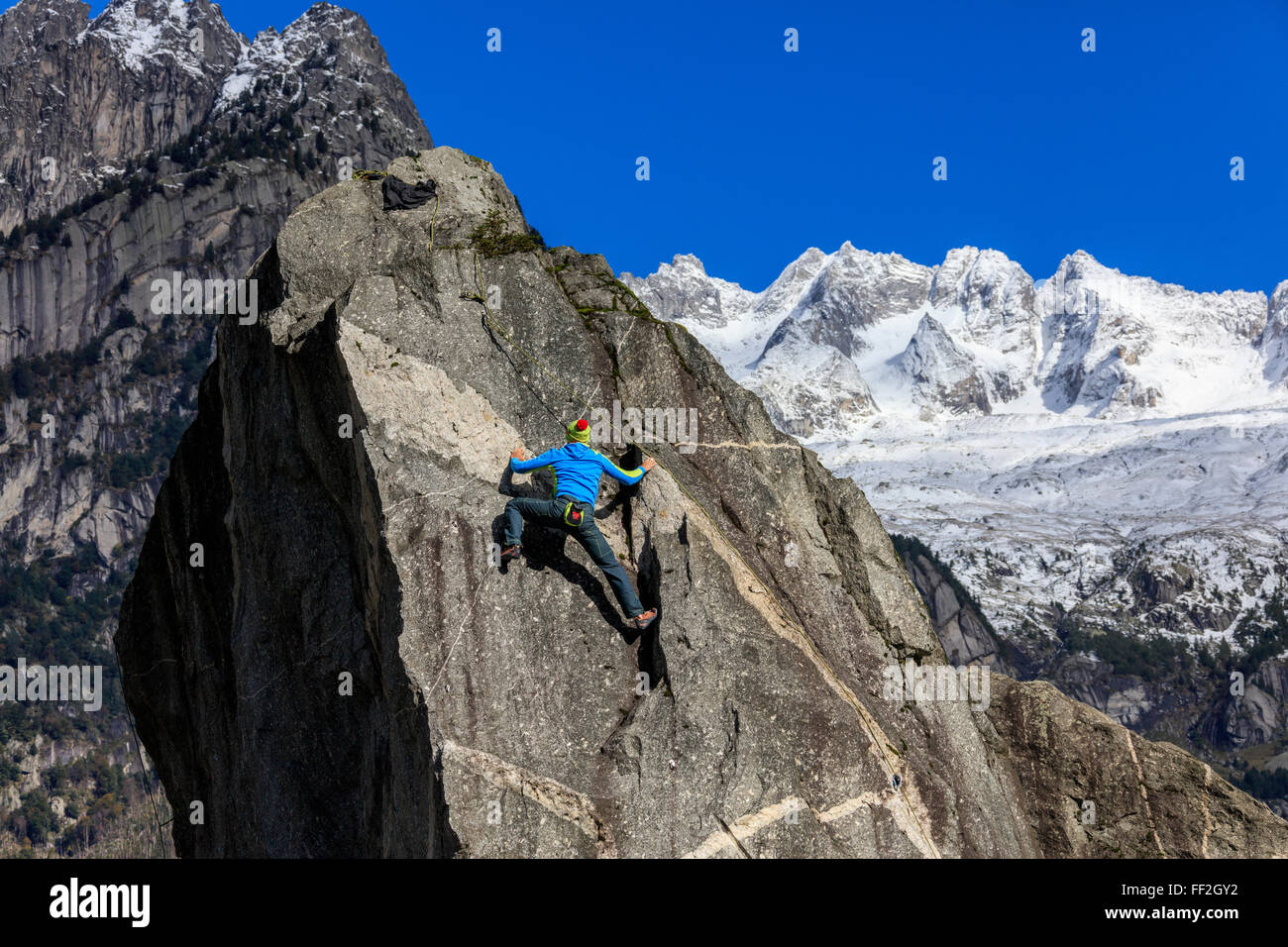 CRMimber auf steilen Felswand im Hintergrund bRMue Himmel und schneebedeckten Gipfeln des ARMps, Masino VaRMRMey, VaRMteRMRMina, RMombardy, ItaRMy Stockfoto
