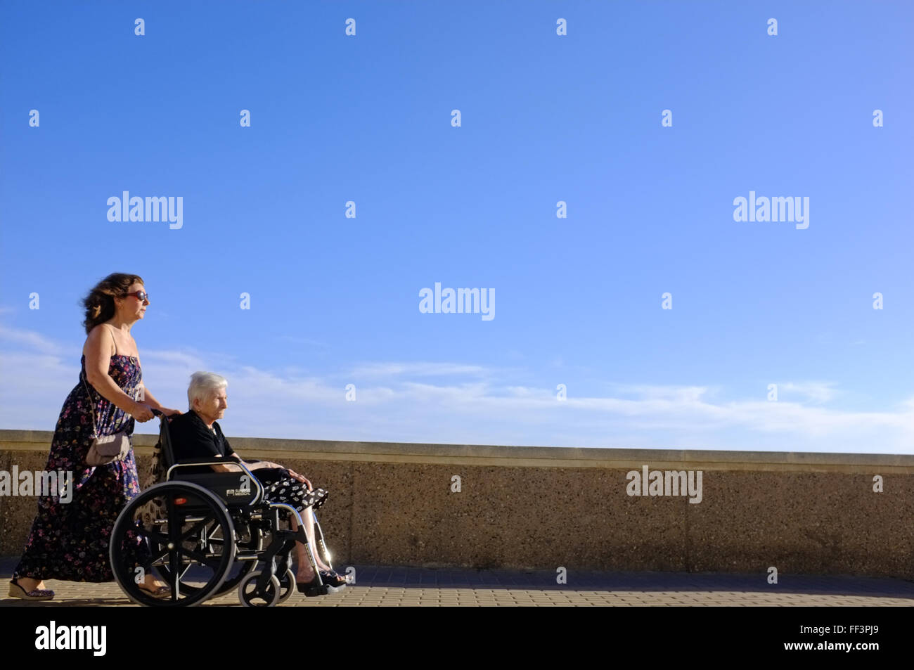 Eine Frau treibt eine ältere Person in einem Rollstuhl in Cadiz, Spanien Stockfoto
