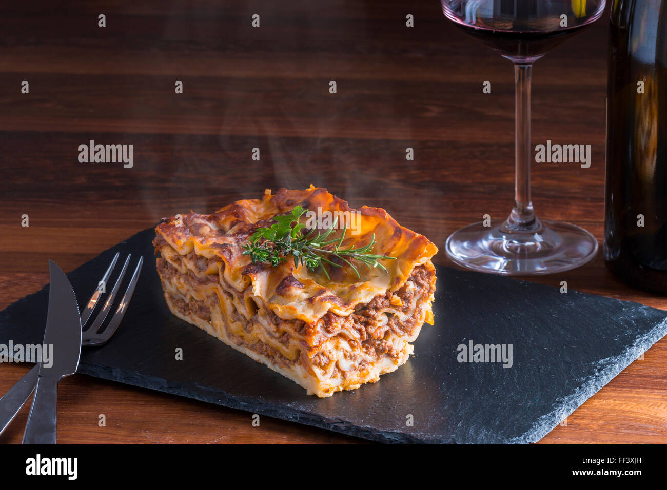 heiß dampfende Lasagne mit Rotwein auf Schiefer und Holz Tisch Stockfoto