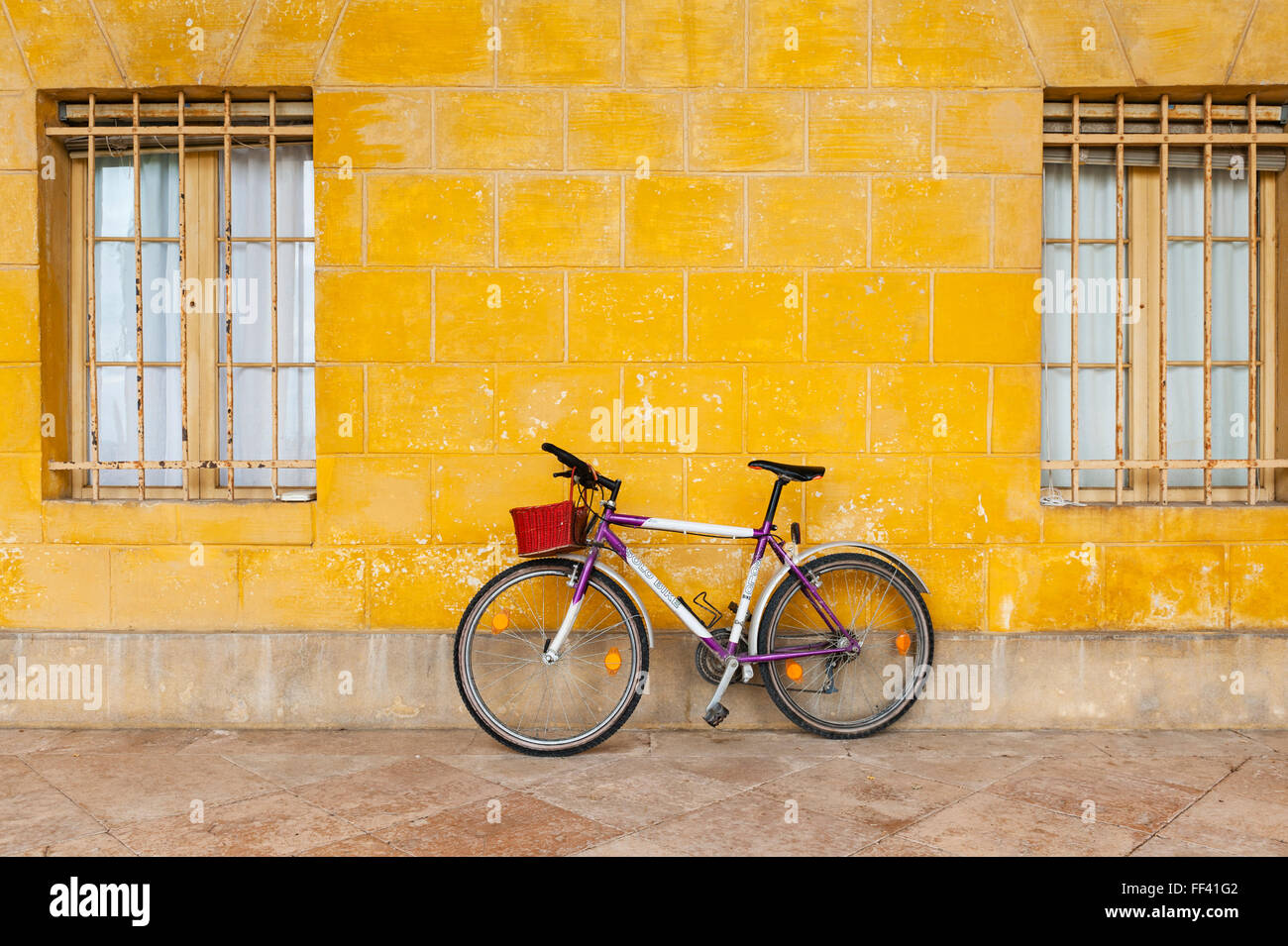 Norditalien. Ein lila Fahrrad mit einem hellen Rot Weidenkorb ein Stuck Wand gelehnt gemalt mit gelben Ocker (Ocker) Stockfoto