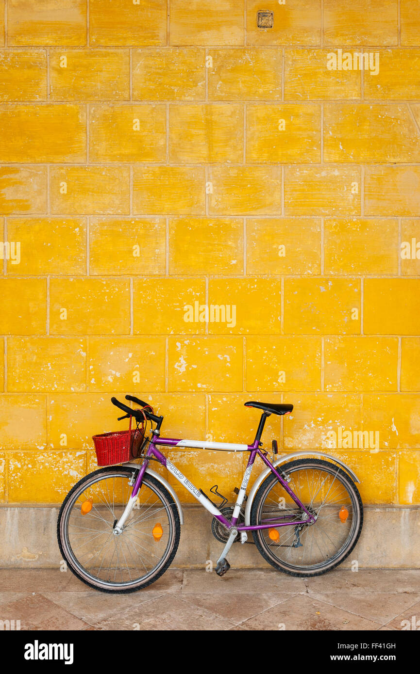 Norditalien. Ein lila Fahrrad mit einem hellen Rot Weidenkorb ein Stuck Wand gelehnt gemalt mit gelben Ocker (Ocker) Stockfoto