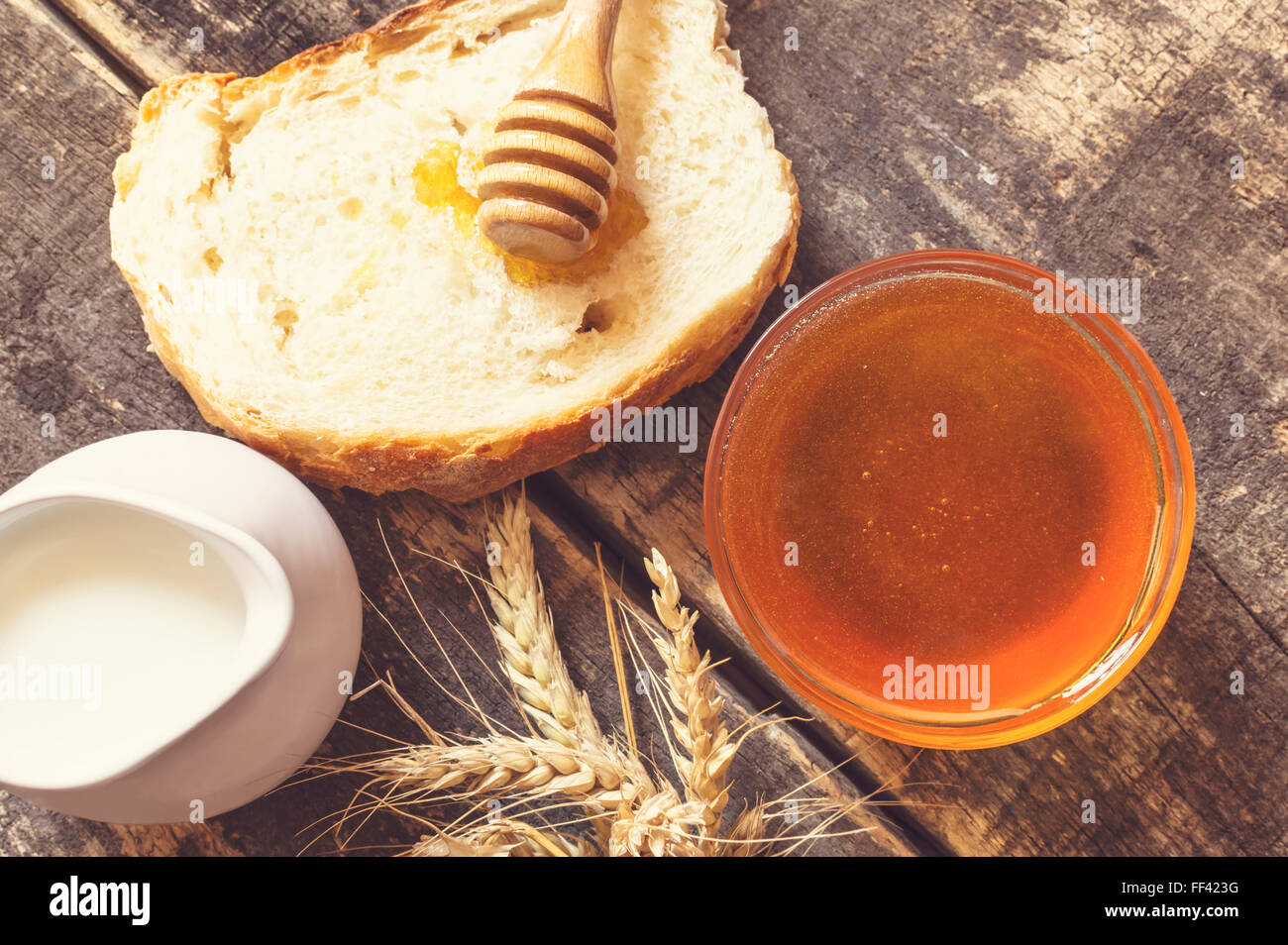 Honig in einem Glas, Scheibe Brot, Weizen und Milch auf einem alten Jahrgang beplankt Holztisch von oben. Frühstück im ländlichen oder rustikalen Stil Stockfoto