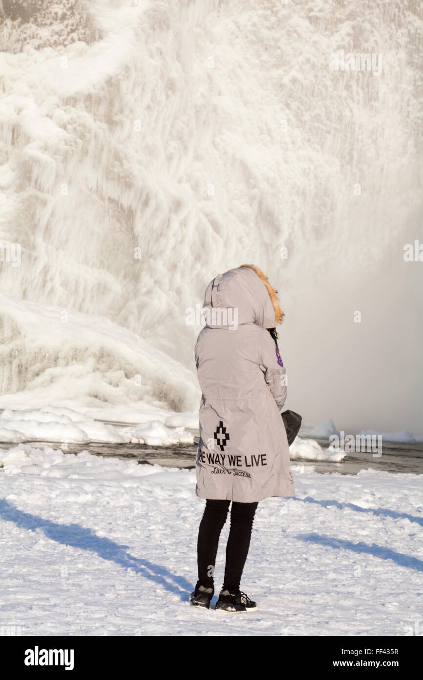 Besucher trägt die Art und Weise wir Leben Glück & Erfolg Mantel am Skogafoss Wasserfall, Island im Januar mit gefrorenen Eiszapfen Stockfoto