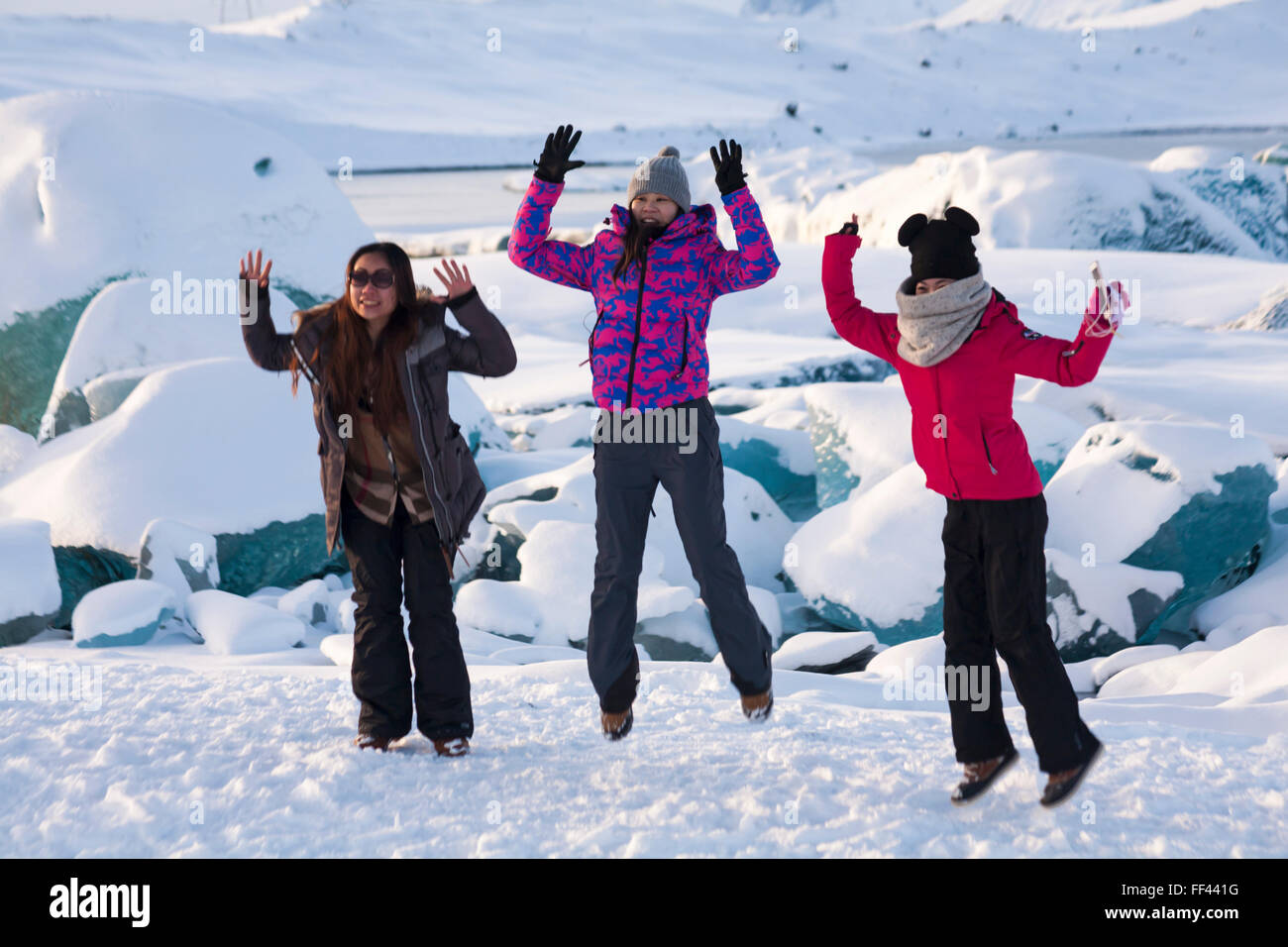 Junge Touristen für Frauen springen im Jokulsarlon Glacial Lagoon, am Rande des Vatnajokull National Park, Island im Januar in die Luft Stockfoto