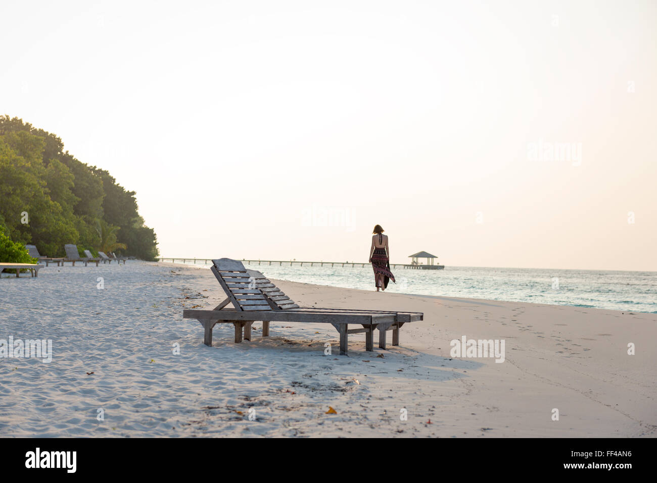 Sonnenaufgang an einem einsamen Strand mit schönen Frau vorbeigehen. einsame Stimmung im warmen Sonnenschein. Stockfoto