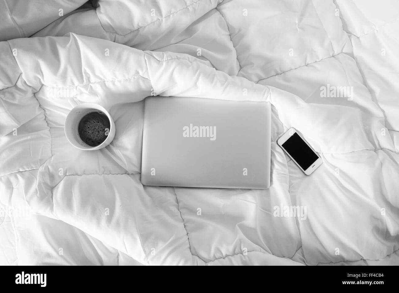 Arbeiten im Bett, Laptop, Smartphone und Tasse Kaffee auf weißen Bett, Morgenlicht Stockfoto