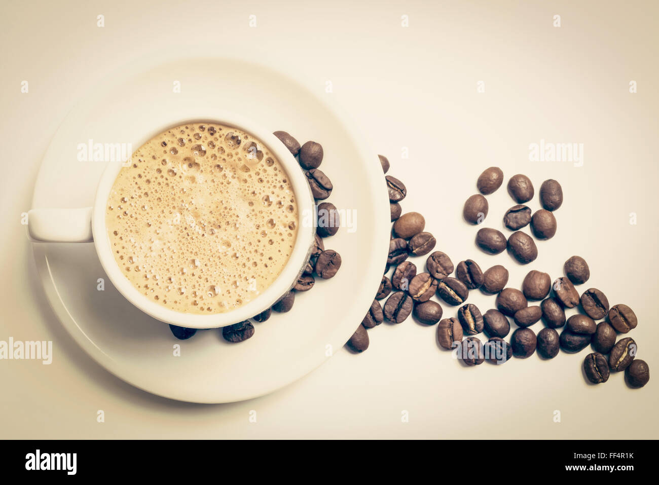 Leckeres Frühstückstasse Kaffee Draufsicht mit Schaum und geröstete Bohne Dekoration, Vintage-Filter. Clipping-Pfad enthalten. Stockfoto