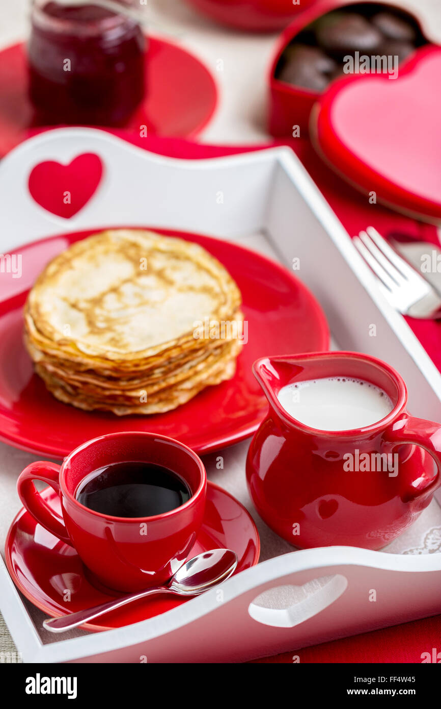 Frühstück. Pfannkuchen und Kaffee mit Milch auf einem Tablett zum Valentinstag. Selektiven Fokus. Stockfoto