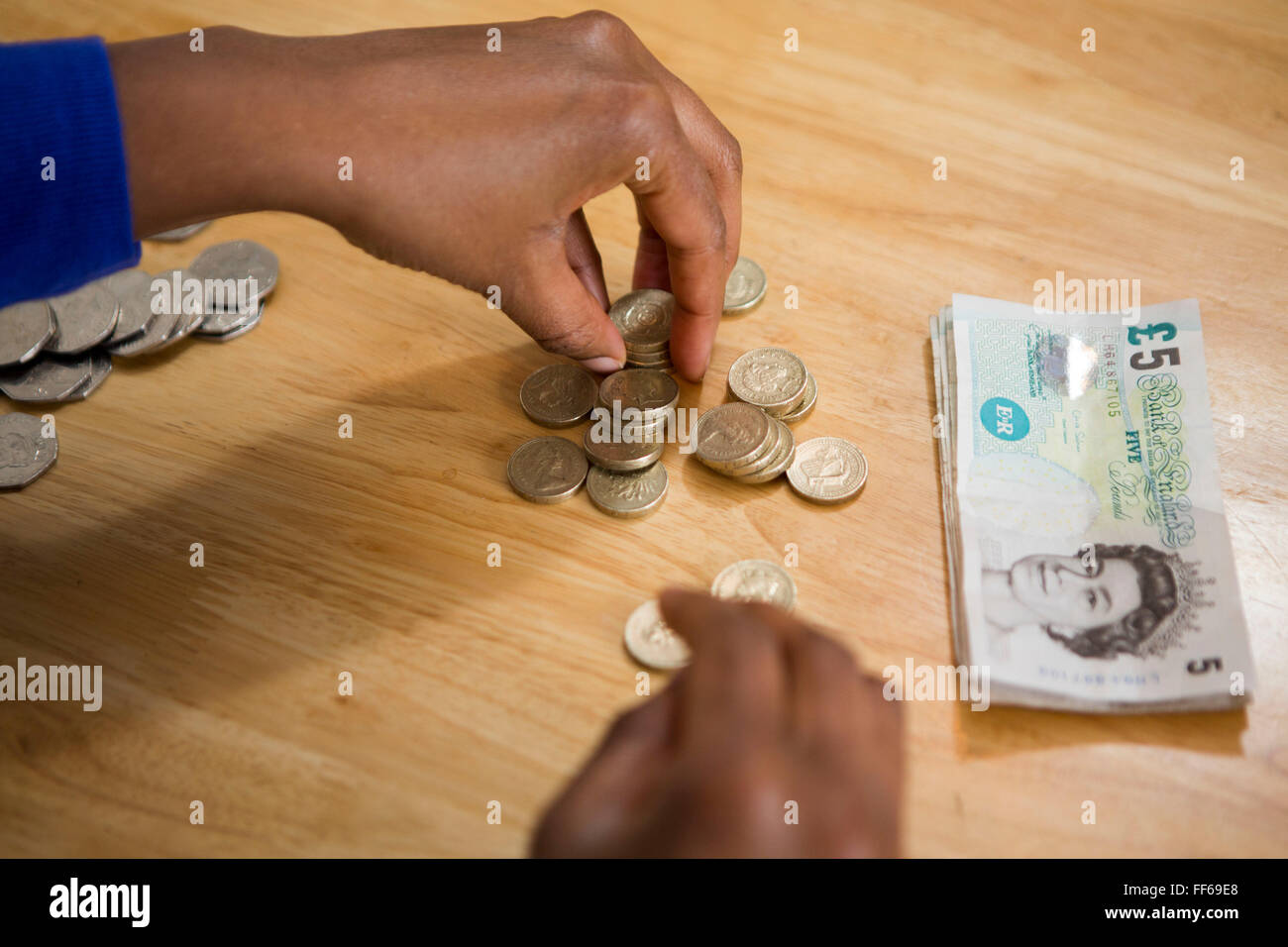 Eine junge Frau sitzt an ihrem Küchentisch zählen ihr Geld um die Haushaltsrechnungen bezahlen. Stockfoto