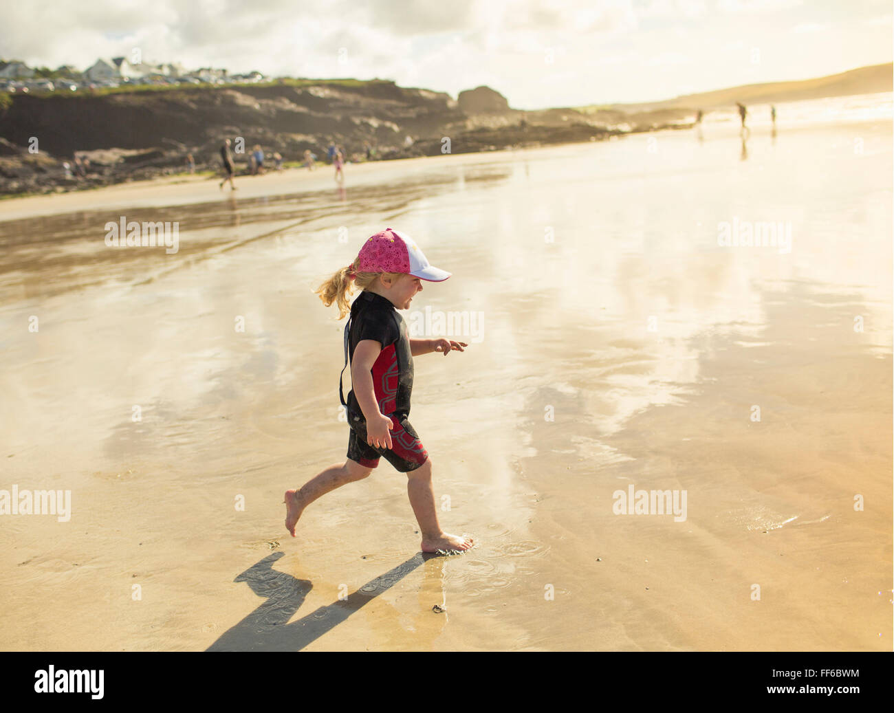Ein Kind in einen Neoprenanzug und Sonnenhut auf Sand laufen Stockfoto