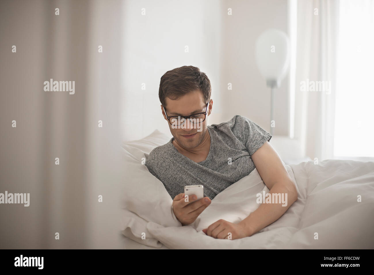 Ein Mann im Bett seine Nachrichten auf seinem Handy. Stockfoto