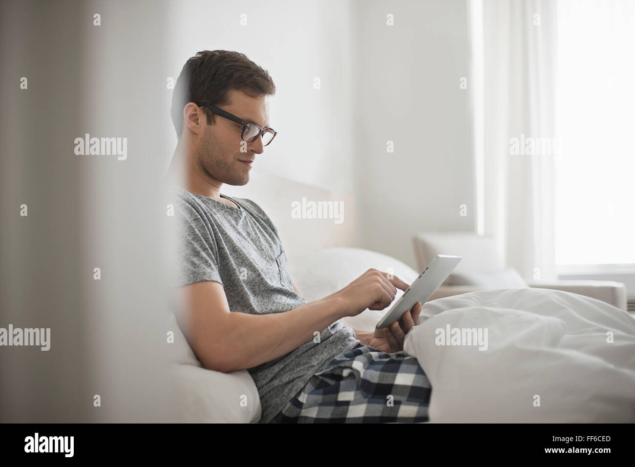 Ein Arbeitstag. Ein Mann sitzt im Bett mit einem digitalen Tablet mit Touchscreen. Stockfoto