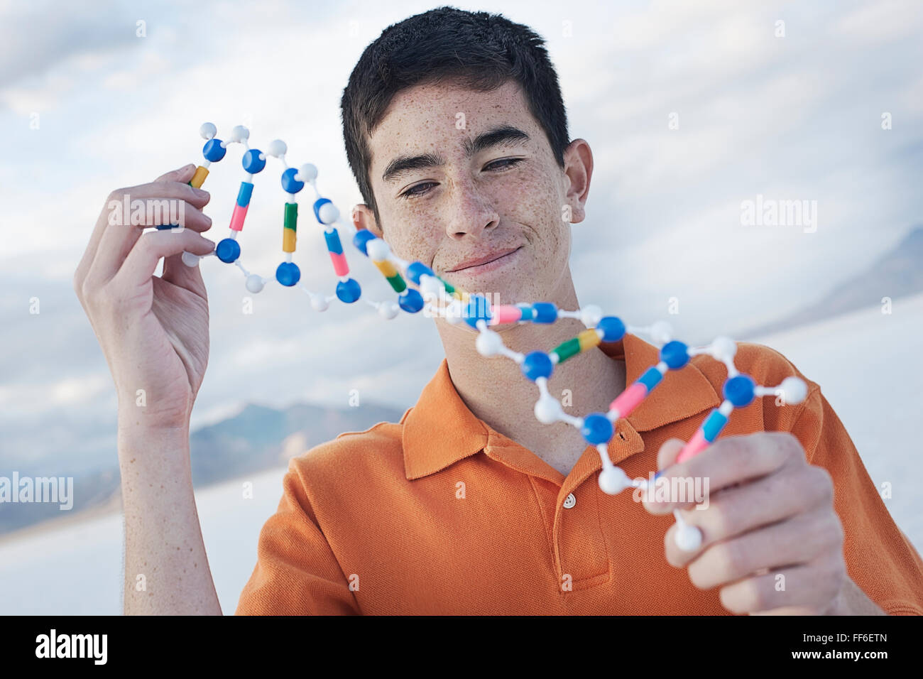 Ein Teenager in eine orange Polo-Shirt, eine molekulare Struktur-Modell hält und es untersuchen. Stockfoto