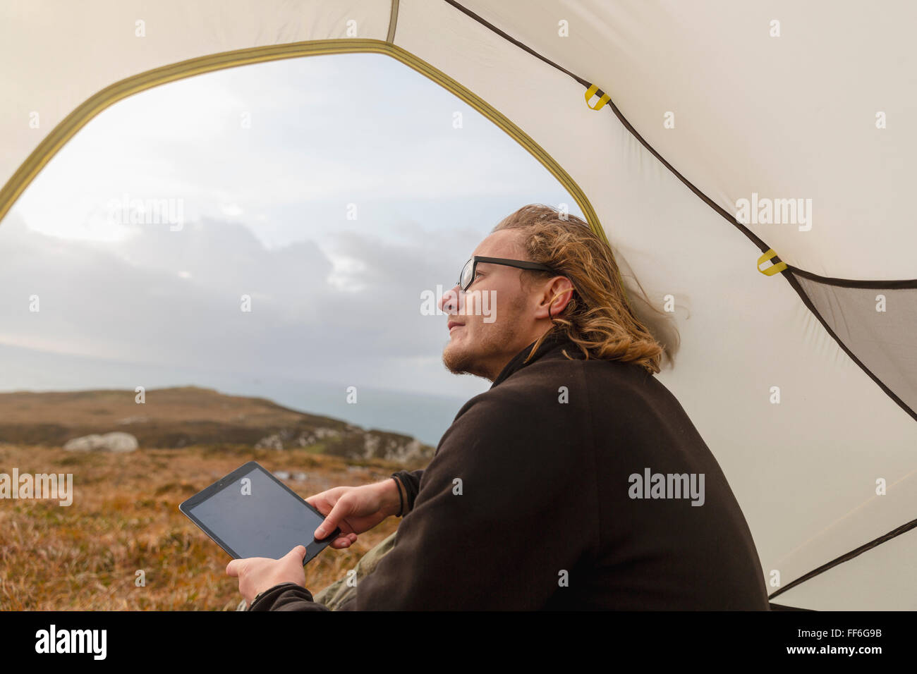 Ein Mann sitzt im Schutz eines Zeltes auf, hält eine digitale-Tablette. Stockfoto