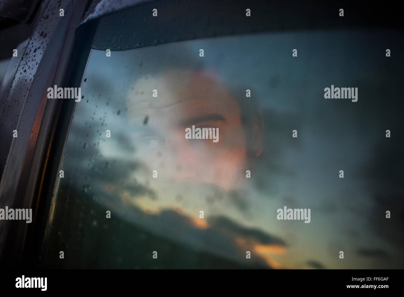 Ein Mann sitzt in einem Auto auf der Suche. Reflexionen auf den Sonnenuntergang Himmel auf das Fenster. Stockfoto