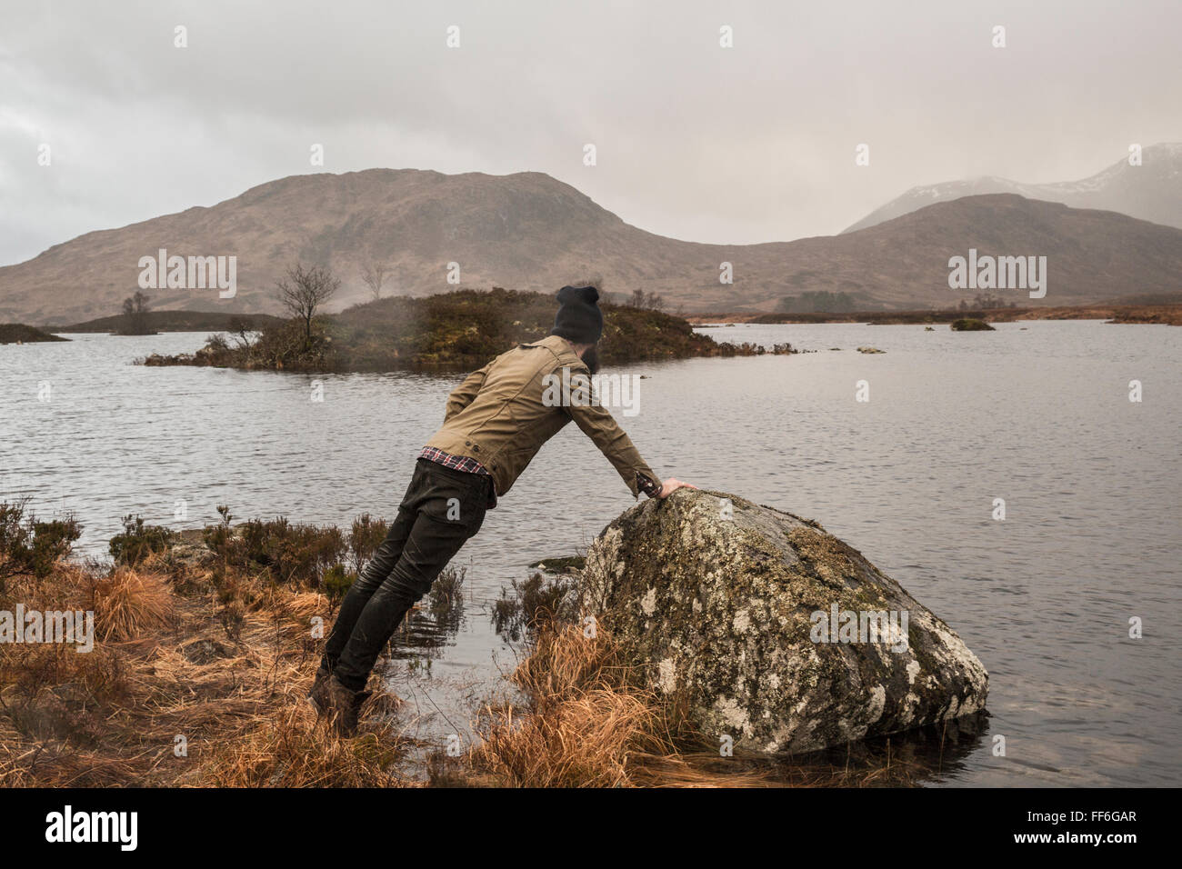 Ein Mann stützte sich auf einem Felsen mit einem Arm und Blick auf einen Kanal über Inseln und Berge. Stockfoto