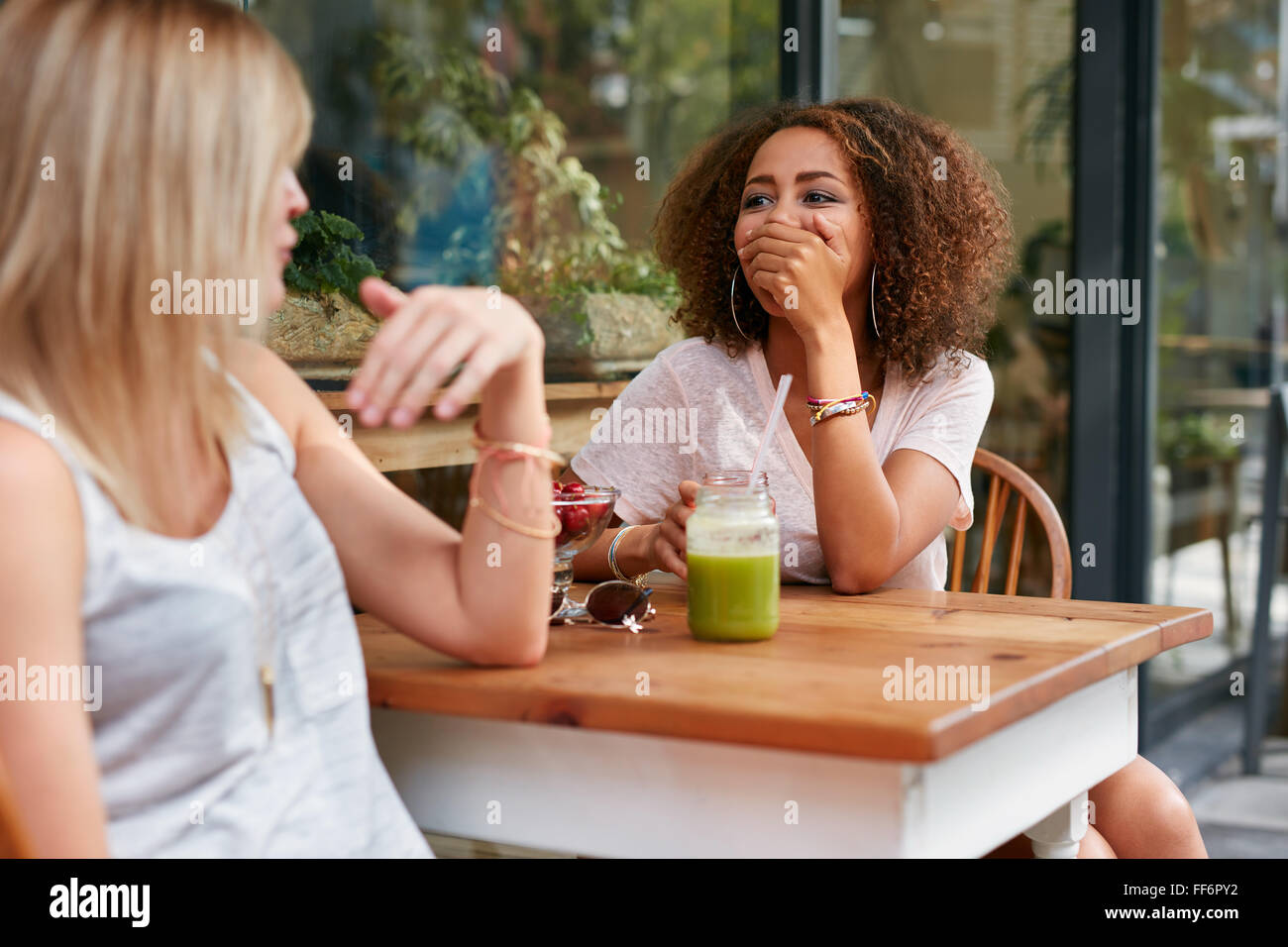 Zwei junge Mädchen im Café im Freien, plaudern und lachen. Freundinnen teilen einige lustige Momente beim Sitzen am Bürgersteig Stockfoto