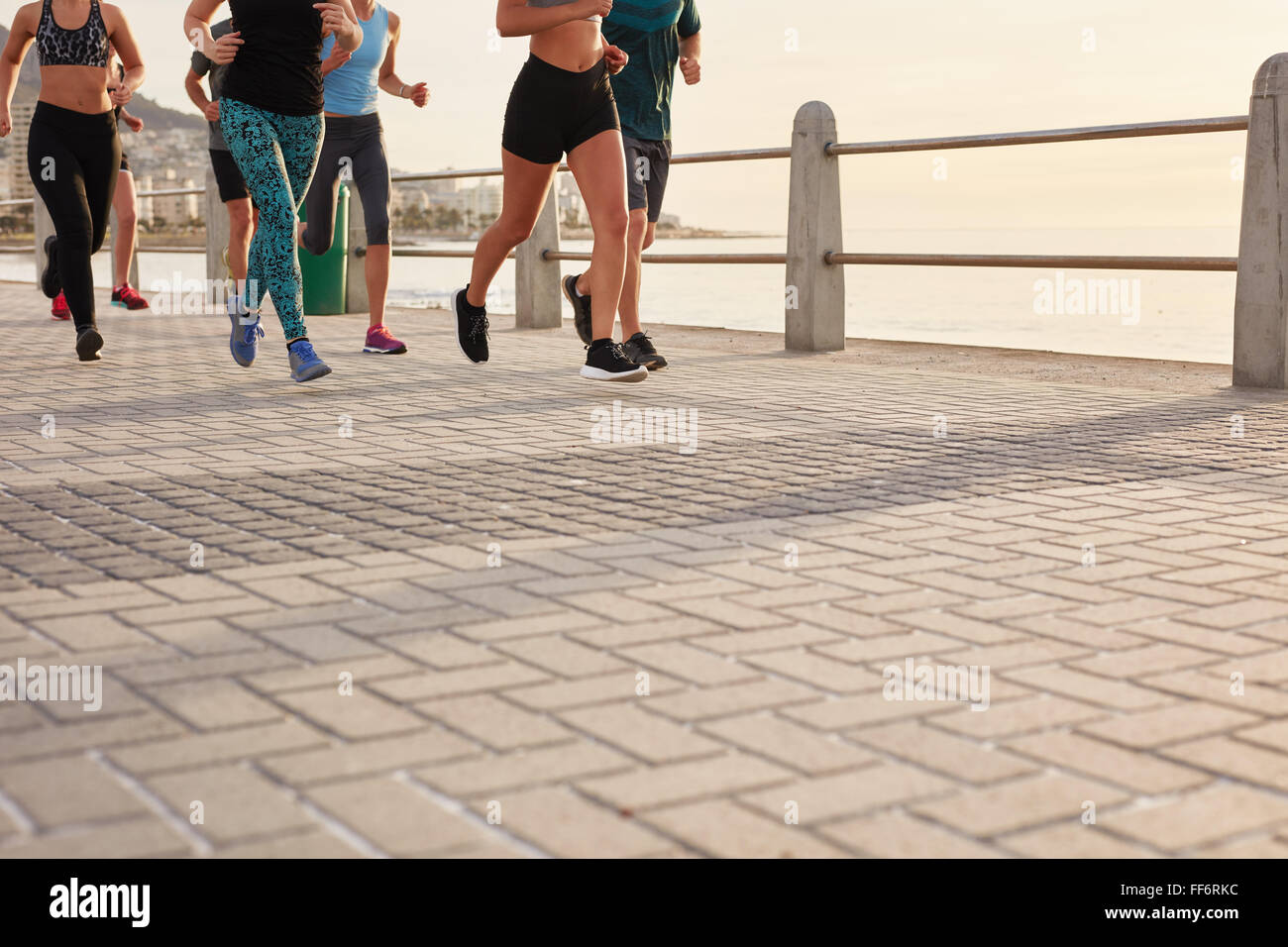 Niedrigen Bereich beschnitten Schuss von Menschen auf der Straße am Meer laufen. Fitnesstraining in der Gruppe direkt an Strandpromenade. Stockfoto