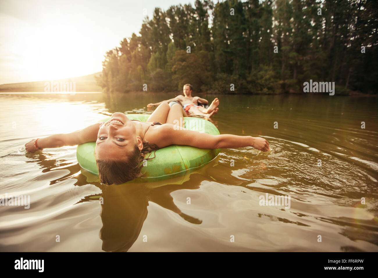 Porträt der lächelnde junge Mädchen in einem Innertube mit einem Mann im Hintergrund in einem See schweben. Junges Paar in See auf inflatab Stockfoto