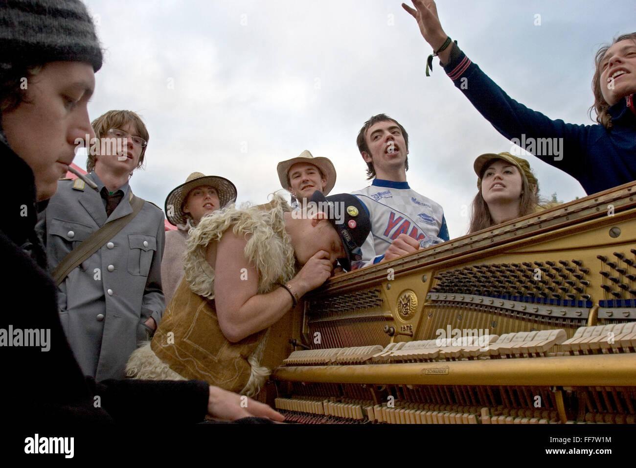 Glastonbury Festival Besucher feiern in das Morgenlicht in Unbestimmtheit verloren. Ein Mann spielt Klavier, Menschen singen und der Mann im mittleren schnaufend Koks aus dem Klavier. Stockfoto