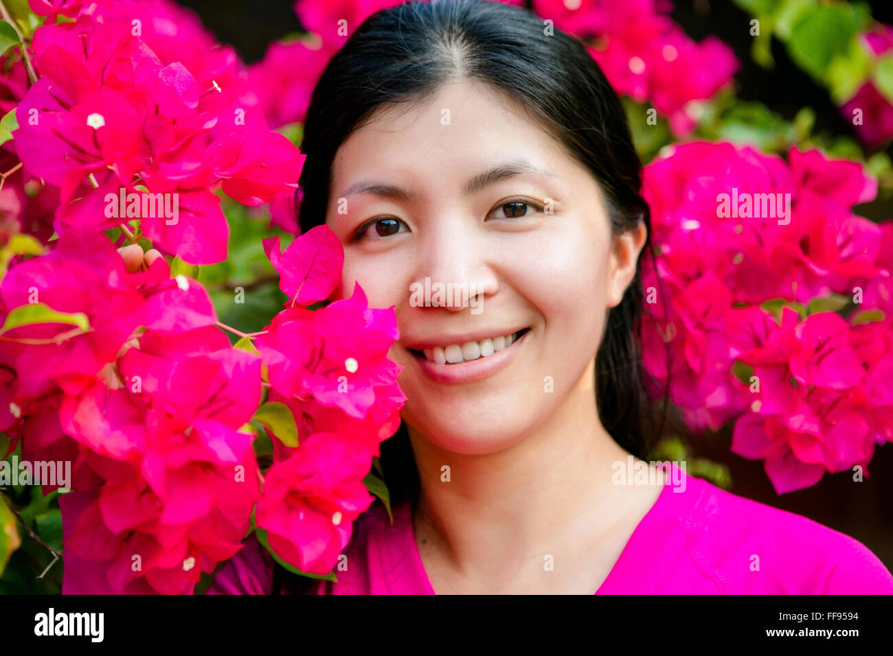 Lächelnden Asiatin neben Rosa Bougainvillea Blumen Stockfoto