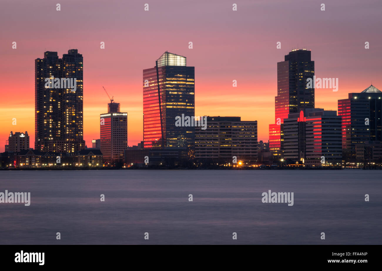 Ein wunderschönen Sonnenuntergang über den Wolkenkratzern von Jersey City und den Hudson River, mit den rosa Himmel spiegelt sich im Wasser. Stockfoto