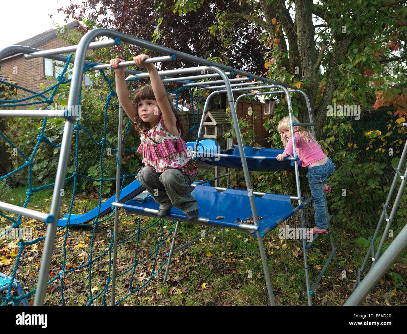 Zwei Mädchen Schwestern auf Klettern umrahmen ein Mädchen auf dem Klettergerüst im Garten England Stockfoto