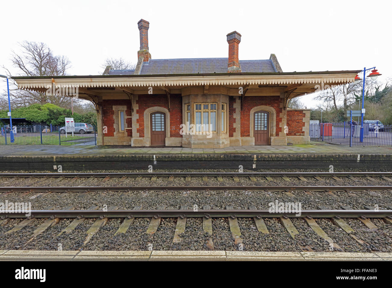 Auf der Suche über die Gleise an einem alten Bahnhof Gebäude mit einem Baldachin aus Holz und Dach mit zwei kunstvollen Ziegelbau Schornsteine geplant. Stockfoto