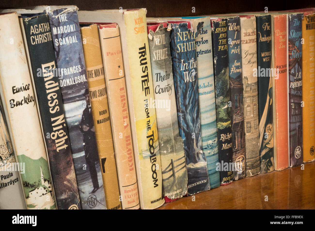 Vintage und Retro-Bücher auf einem braunen Holzregal, einschließlich Autoren wie Nevil Shute, Agatha Christie und Frances Donaldson. Stockfoto
