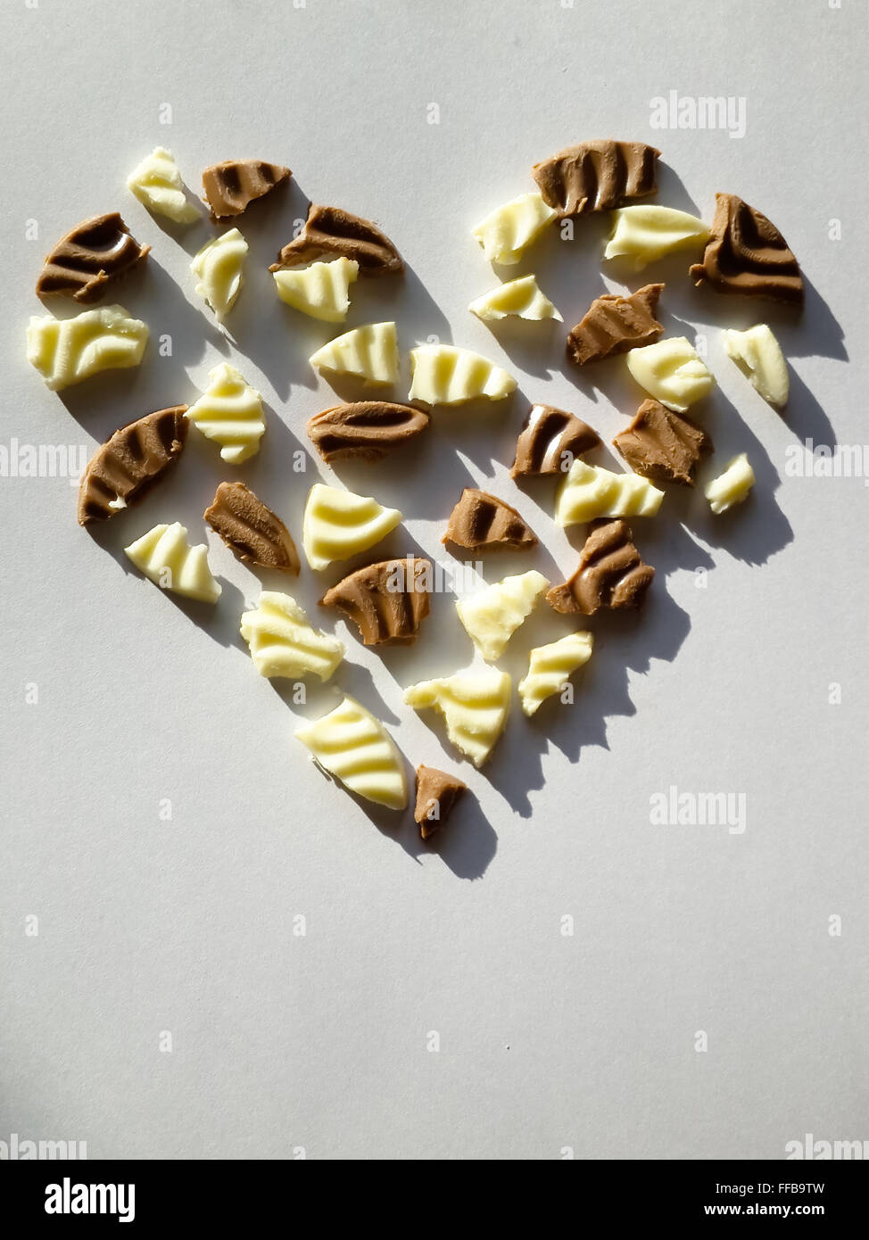 Herzform gemacht von weißer und dunkler Schokolade Fragmente auf weißem Hintergrund. Hartes Licht und Schatten-Einstellung. Stockfoto